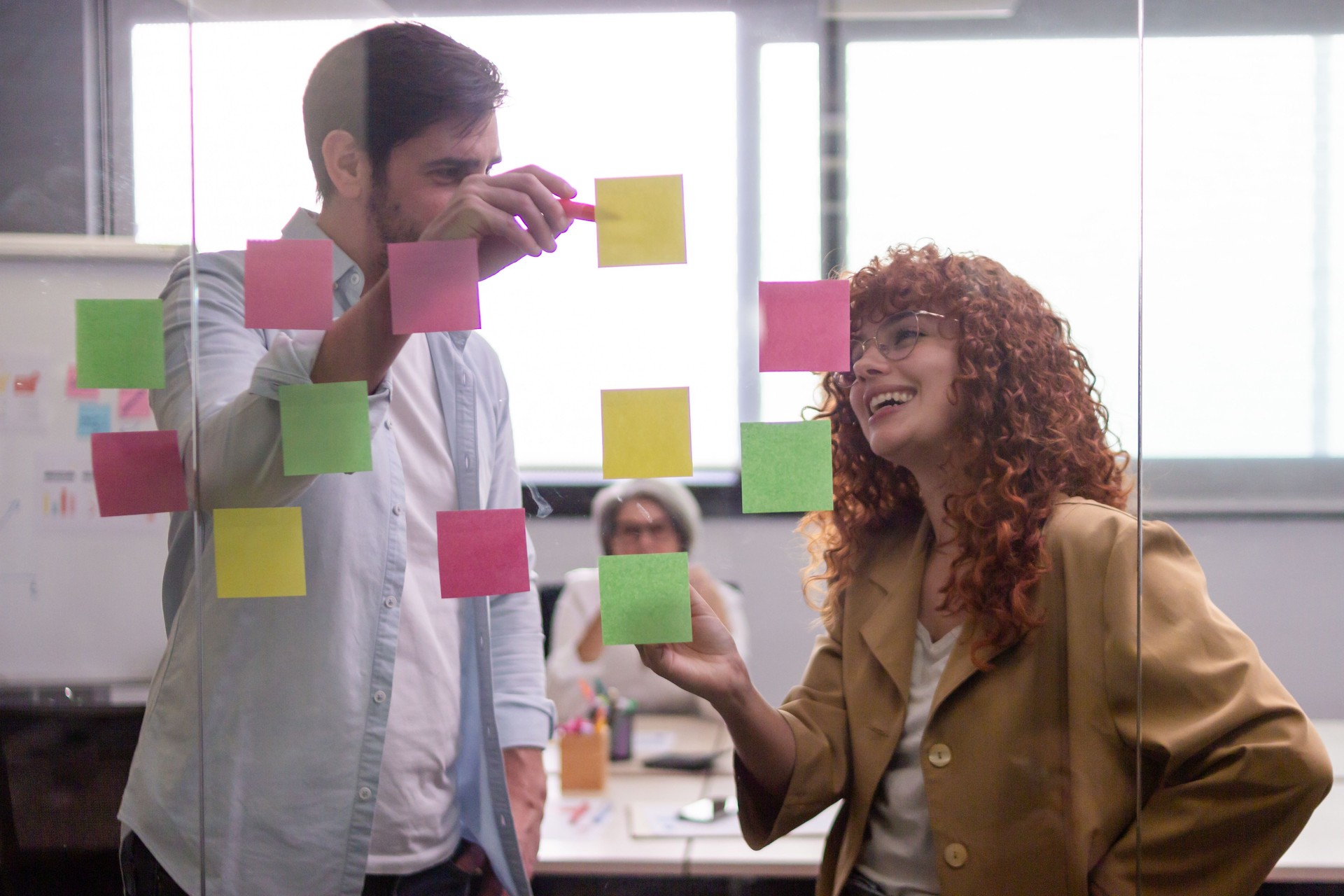 Coworkers planning strategy using sticky notes on glass wall in office